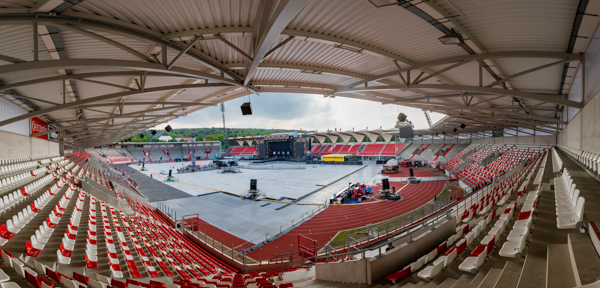 Blick von den &uuml;berdachten Trib&uuml;nen auf das Steigerwaldstadion mit aufgebauter B&uuml;hne und leeren Sitzreihen vor einem Open-Air-Konzert